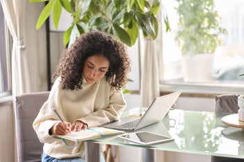 female student with curly hair using laptop at home office, natural sunlight and modern desk