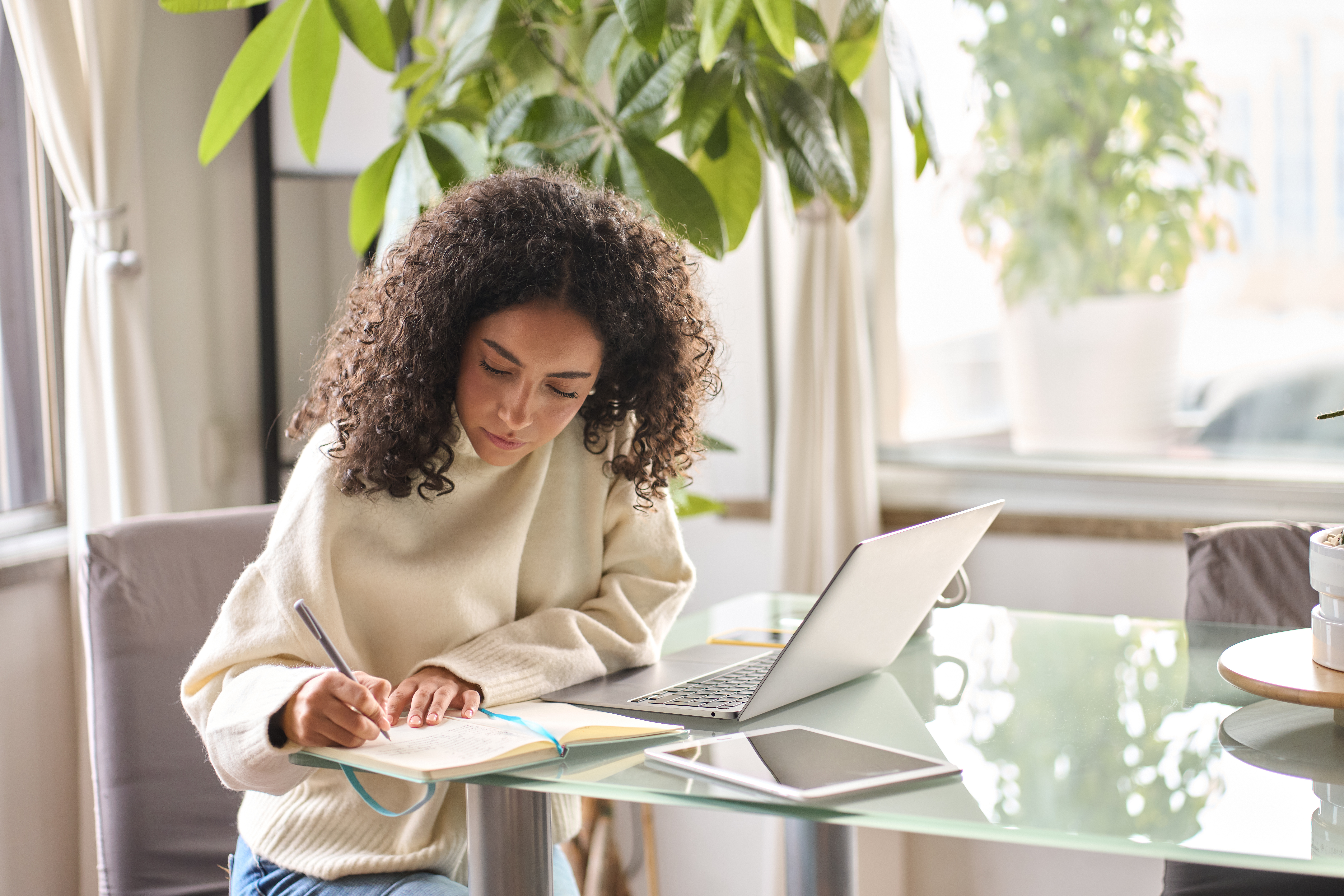 female student with curly hair using laptop at home office, natural sunlight and modern desk